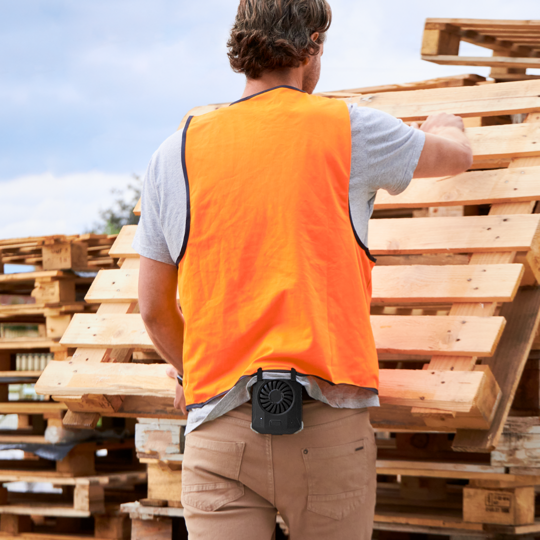 Person working outdoors, lifting a pallet while wearing a portable cooling fan on waist